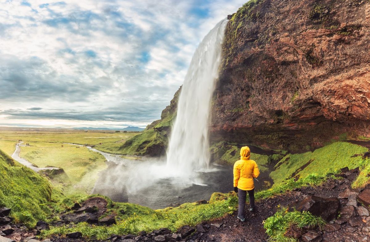 A hiker in a yellow jacket beside Seljalandsfoss waterfall in Iceland