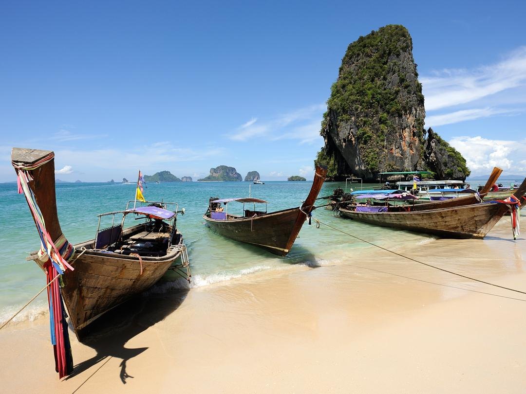 Longtail boats on a beach beneath limestone cliffs in Krabi, Thailand