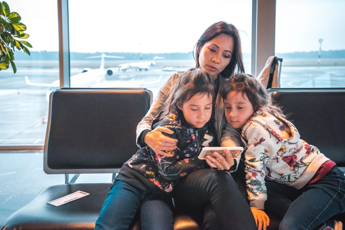 A parent and two children looking at a phone together at an airport gate