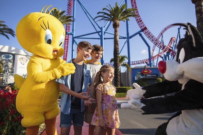 Children meeting cartoon characters at a theme park with a roller coaster behind